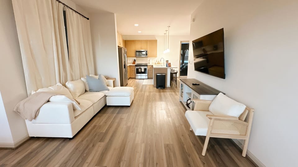 Bright living area with sectional sofa and TV, opening directly into the kitchen.