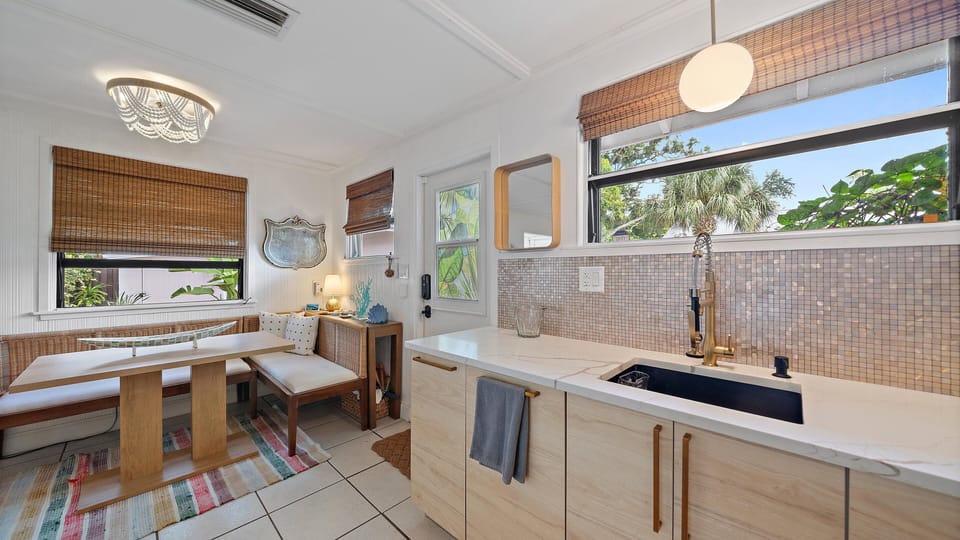 Enjoy your morning coffee in this bright kitchen nook, featuring coastal-inspired décor, modern finishes, and lush garden views through the windows.