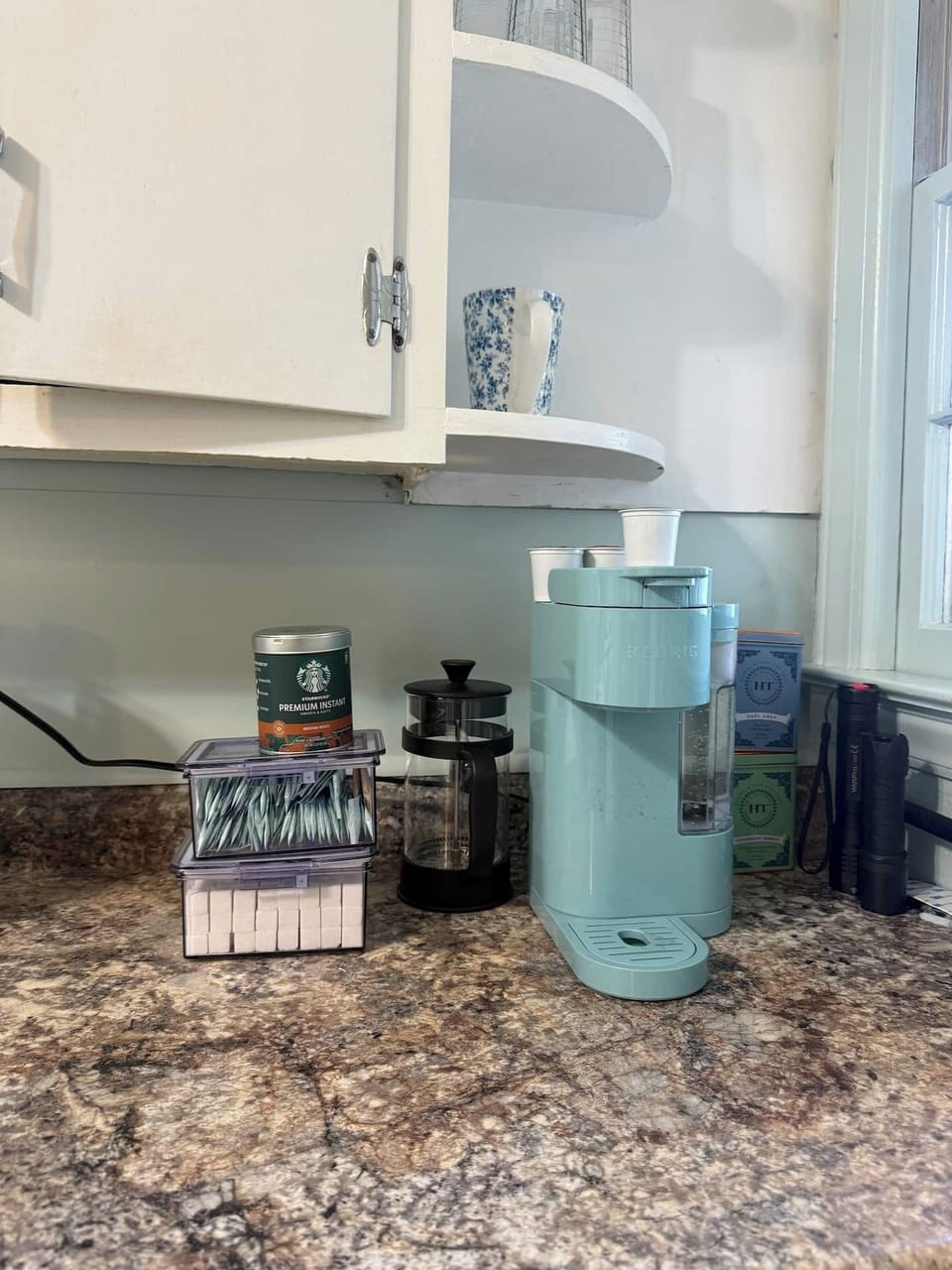 Coffee station arranged with single serve brewer French press and assorted supplies for guest use.
