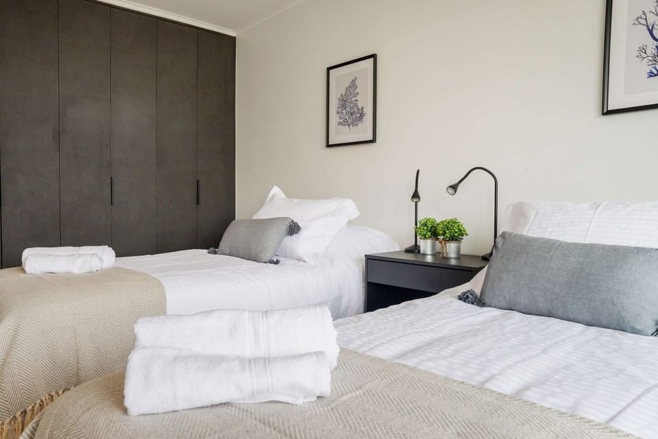 Unwind in this stylish bedroom featuring cozy twin beds, modern decor, and ample storage space for a relaxing stay.