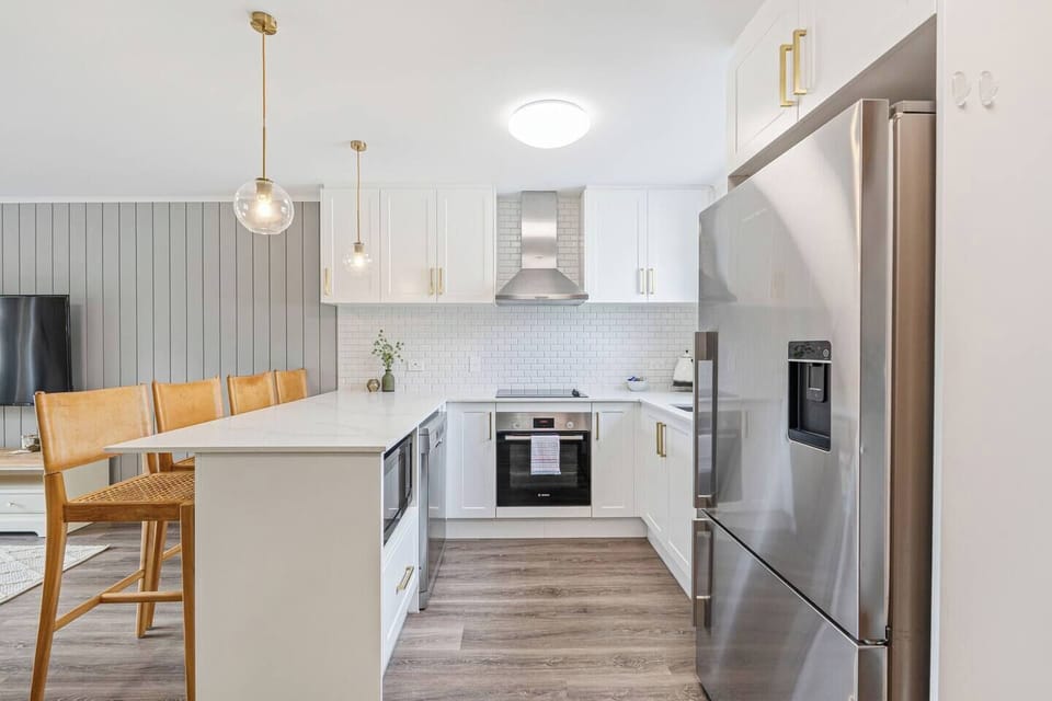 The sleek kitchen features crisp white cabinetry and quality appliances, including a full-size fridge with ice maker, oven, cooktop, microwave, dishwasher, kettle, toaster, and coffee essentials.