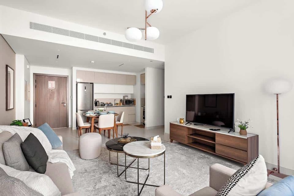 Spacious living room featuring a large convertible sofa bed, stylish center coffee table, comfortable armchair, and a 65-inch TV screen for your entertainment. Overlooking the Dining area and Kitchenette. 