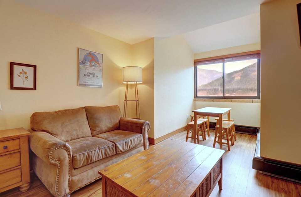 Comfortable sitting area featuring a plush sofa, rustic wood coffee table, and a dining nook by the window with views of the surrounding mountains. Perfect for relaxing après-ski.