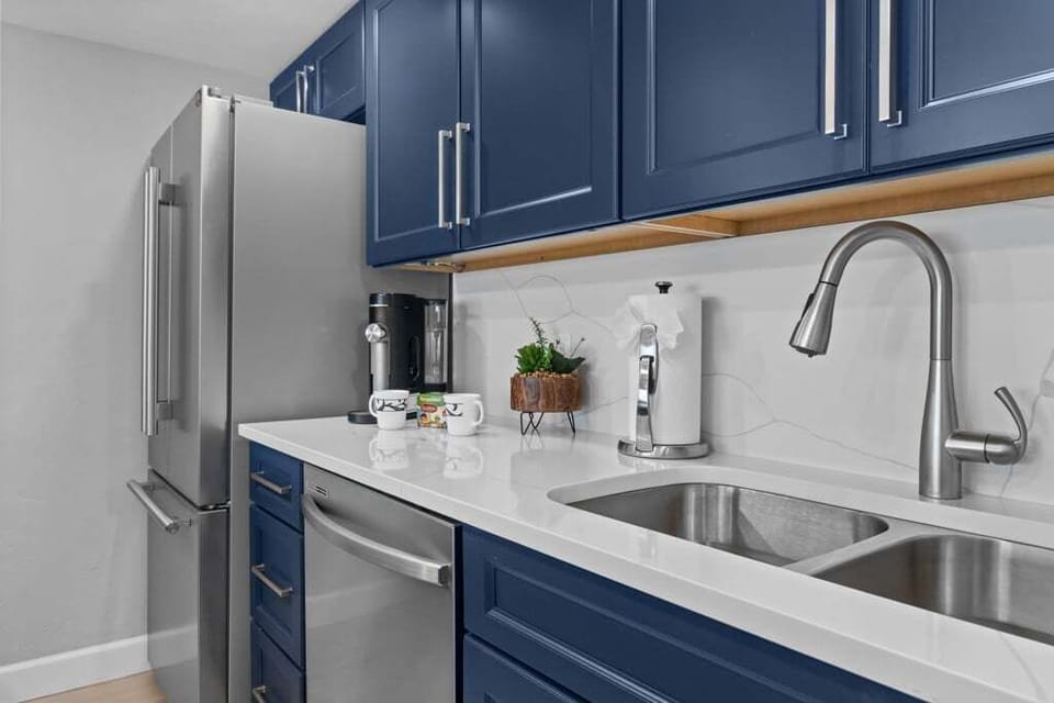 Modern kitchen with bold navy cabinetry, sleek stainless steel appliances, and a stylish breakfast bar with plush seating—perfect for cooking, dining, and entertaining.