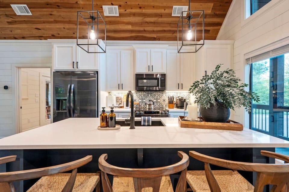 This kitchen is seriously a dream to cook in with those huge windows overlooking the trees, sleek black appliances, and enough counter space that you could actually prep a real meal without bumping elbows with everyone else.