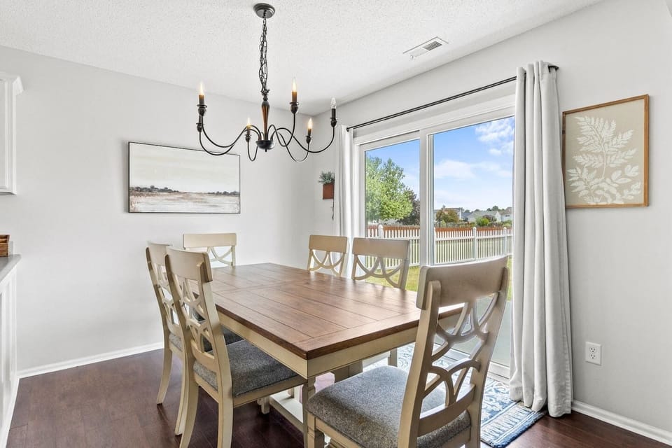 Enjoy family meals or casual brunches at this elegant wooden dining table with cushioned seating for six, bathed in natural light from the sliding glass doors.