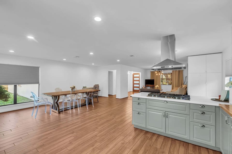 Large wooden table seats up to 8, accented by clear modern chairs and a picture window with views of the yard.