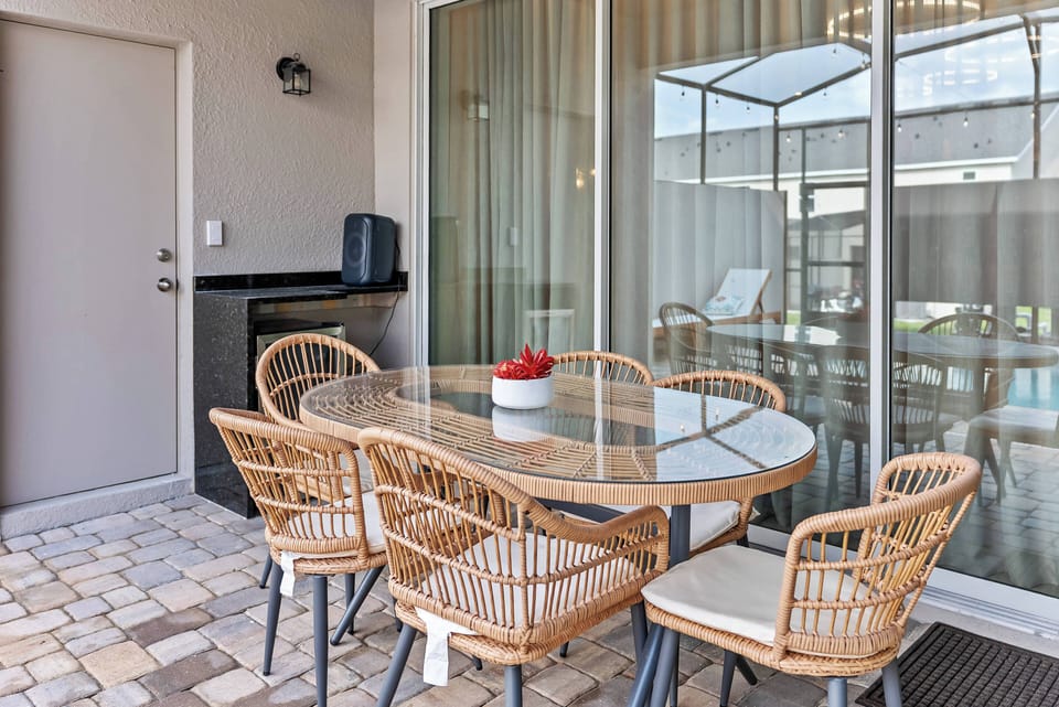 Step outside to a lovely dining area with a sleek glass table and stylish wicker chairs, ideal for al fresco meals. Natural light flows through large glass doors, creating a warm and inviting atmosphere for guests.