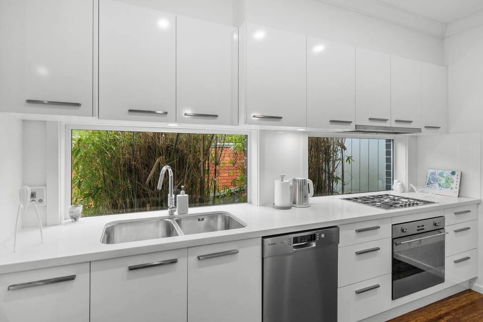 Cook with ease in the fully equipped kitchen, offering a gas cooktop, oven, dishwasher, Nespresso machine, full-size fridge, and leafy views through the wide splashback windows.
