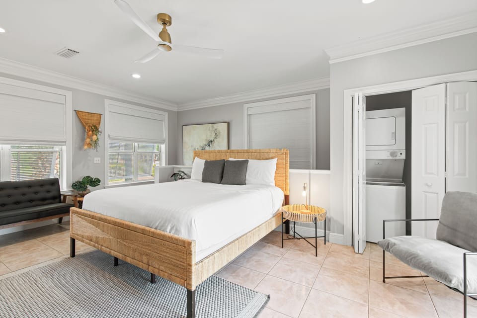 Sink into crisp white linens on your stylish woven bed while natural light streams through bamboo blinds, creating the perfect retreat.