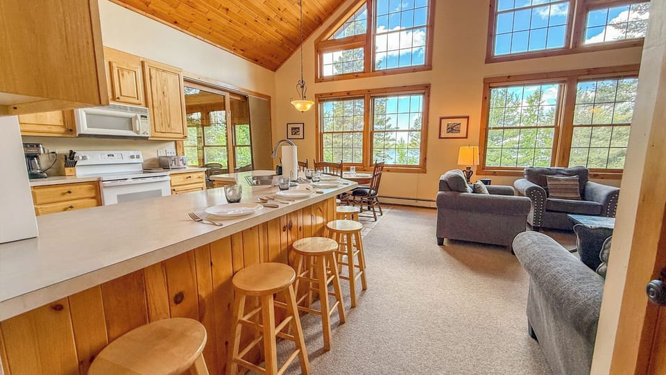Sunlight pours through soaring windows into your open-concept living space, where you can cook, dine, and relax together. The natural wood and cozy seating invite you to unwind after a day of adventure.