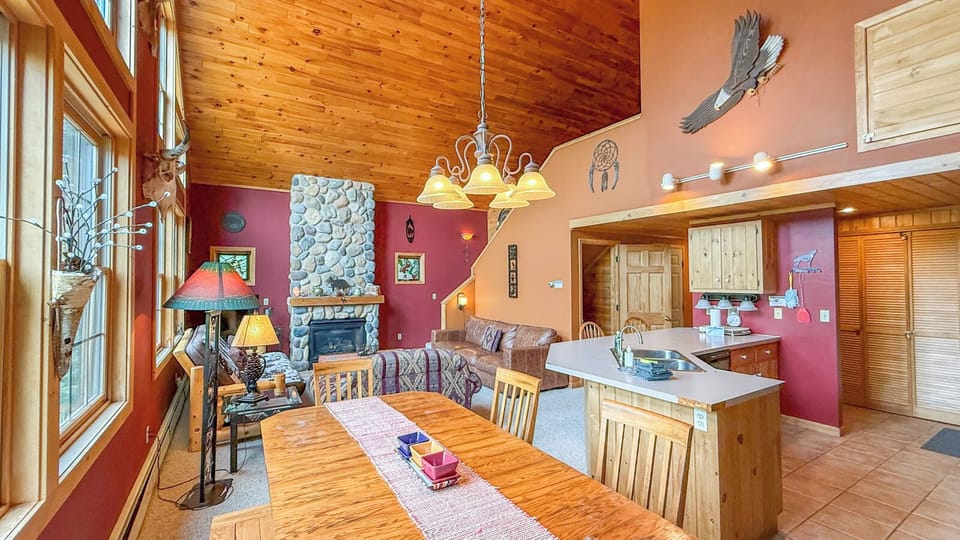 Gather around the warm wood dining table in your spacious lodge-style retreat, where soaring pine ceilings, rustic décor, and a cozy stone fireplace create a welcoming mountain escape perfect for memorable meals and conversation.