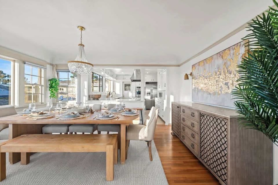 Natural wood finishes create a warm, earthy vibe, while a richly detailed buffet table adds character to the space. White walls and ceiling allow the expansive windows to flood the room with natural light, making it feel bright and airy.