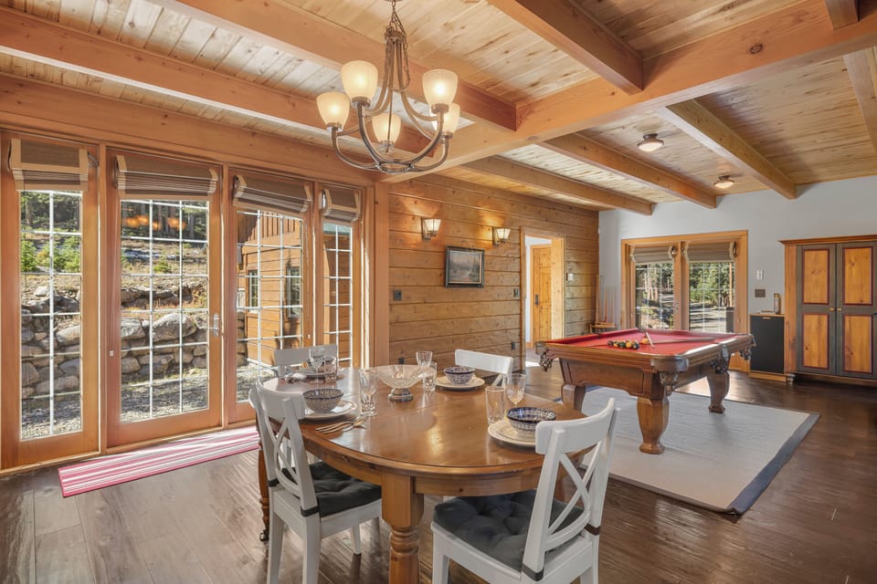 Open-concept living and dining area - with cozy couches centered around a soapstone woodstove, a smart tv, sound system, the billiard table, and a central dining table with comfortable seating for 4.