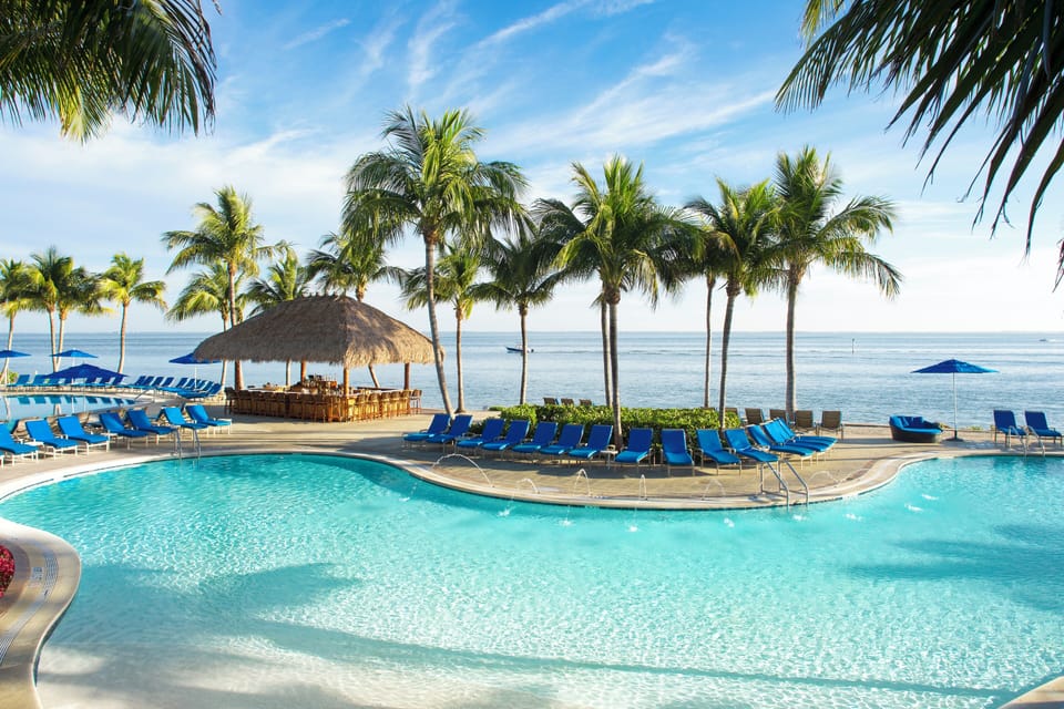 Lounge under swaying palms with serene waterfront pool views.