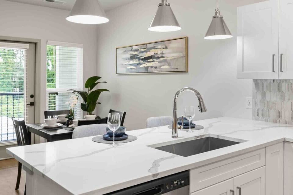 Kitchen & Dining View-Bright kitchen island with sleek countertop and modern fixtures overlooking a dining area set for four. Natural light and open layout make it ideal for meals and entertaining.