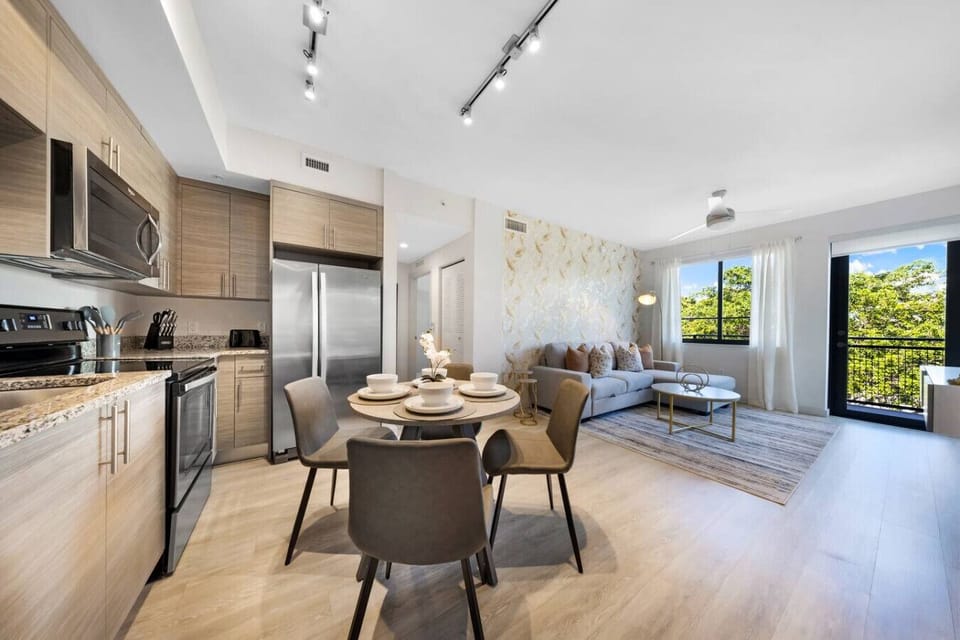 Open-Concept Living & Dining- Modern open layout with a fully equipped kitchen, dining area, and bright living room featuring large windows and balcony views. Perfect for relaxing or entertaining.