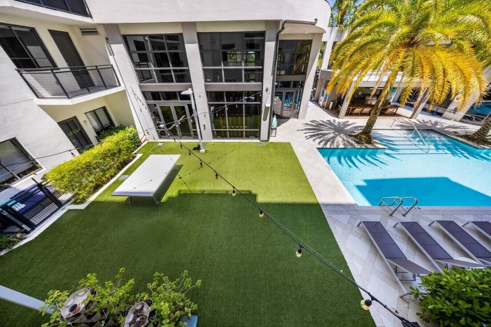 Courtyard with Games and Pool-Lively outdoor space featuring a green lawn with ping pong table, string lights, and poolside lounge chairs. Perfect for relaxation and fun under the sun.