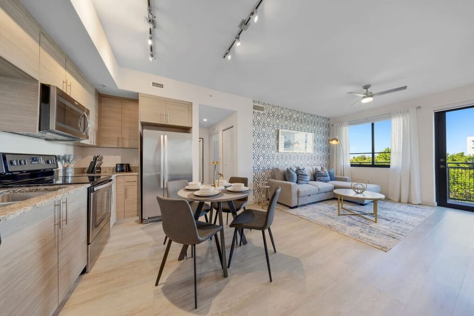 Open Dining and Living Space-Modern open-concept layout with a fully equipped kitchen, dining table for four, and stylish living area. Bright windows and balcony access create a welcoming atmosphere.