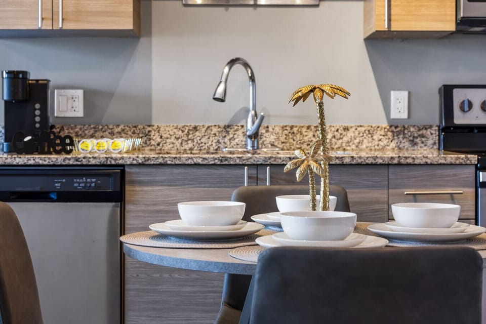 Stylish Kitchen & Dining Setup-Modern kitchen with granite counters and stainless appliances. Dining table set with chic dishware and a gold palm centerpiece, creating a warm and elegant dining experience.