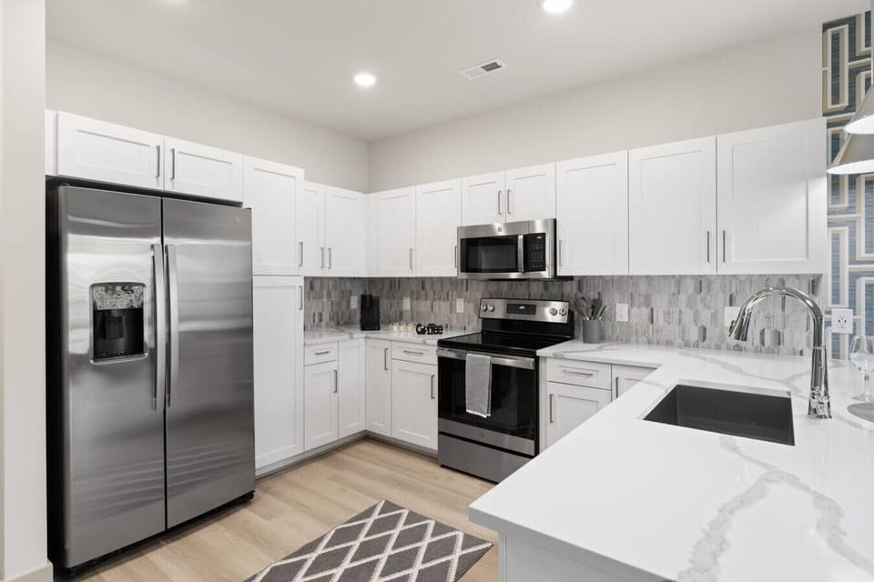 Sleek Fully Equipped Kitchen-Modern kitchen with stainless steel appliances, ample white cabinetry, and stylish backsplash. Features a spacious breakfast bar, pendant lighting, and everything needed for a comfortable stay.