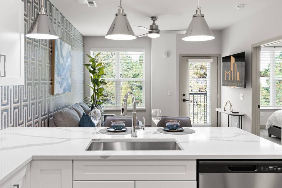 Bright Kitchen with Open View-Modern kitchen island with sleek countertops and pendant lighting overlooking the living room. Large windows and balcony access bring in natural light, creating an airy open-concept space.
