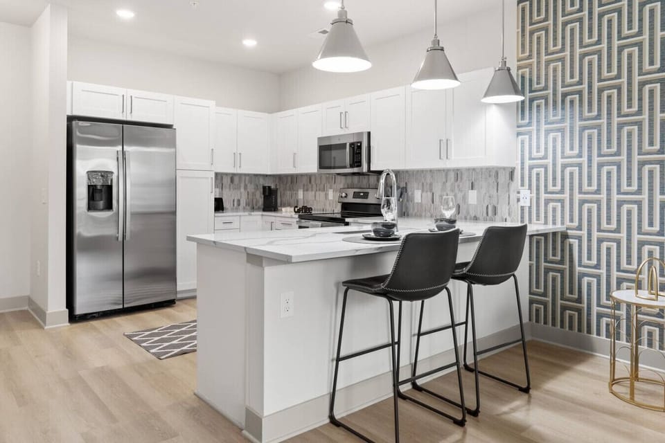 Stylish Kitchen with Breakfast Bar-Bright modern kitchen with stainless steel appliances, white cabinetry, and chic backsplash. A spacious island with bar seating creates the perfect spot for casual dining or morning coffee.