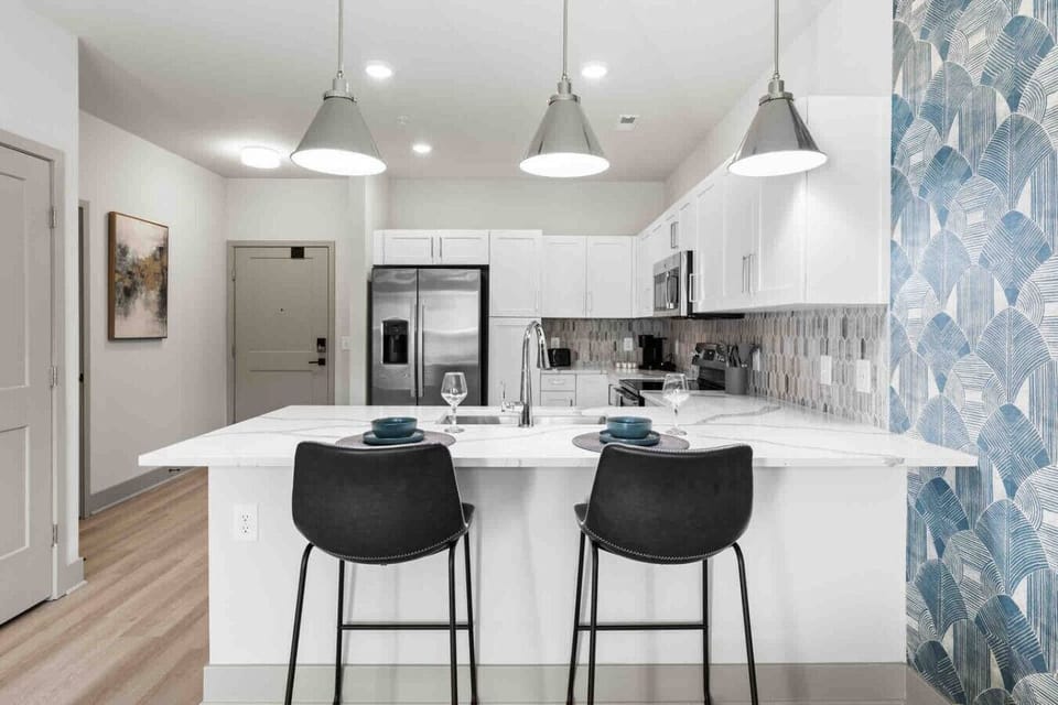 Kitchen with Breakfast Bar-Modern kitchen with stainless steel appliances, white cabinetry, and stylish backsplash. Features a spacious island with bar seating, perfect for dining or entertaining.