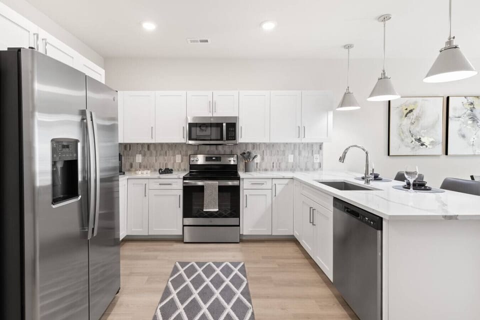 Modern Kitchen-Stylish kitchen with stainless steel appliances, white cabinetry, and sleek countertops. Complete with bar seating and pendant lighting, perfect for cooking and entertaining.