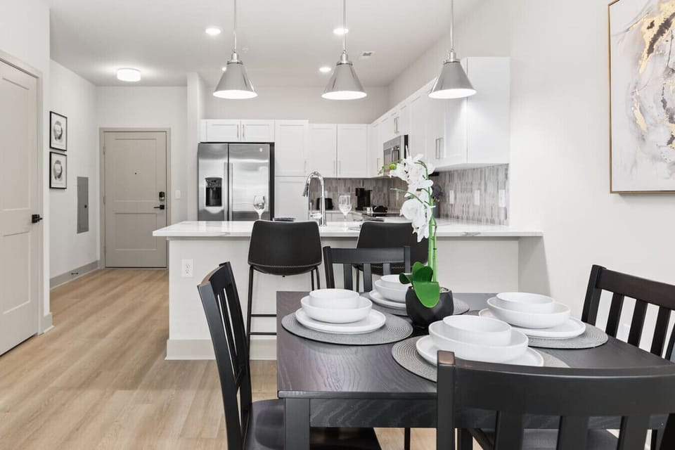 Stylish Dining & Kitchen-Modern dining table set for four, complemented by a sleek kitchen with stainless steel appliances and bar seating. Bright lighting and open design create a welcoming atmosphere.
