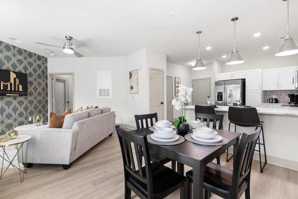 Open Dining & Kitchen Space-Inviting dining area with modern tableware, open to a sleek kitchen with stainless steel appliances and bar seating. Ideal for shared meals and gatherings in a bright, contemporary setting.