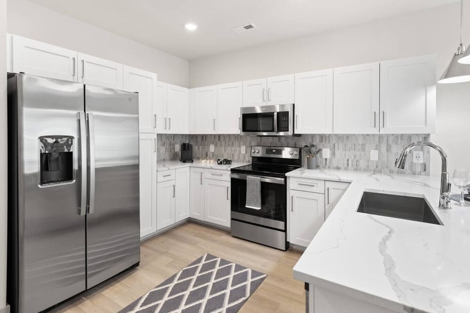 Modern Kitchen-Stylish kitchen with stainless steel appliances, white cabinetry, and sleek countertops. Complete with bar seating and pendant lighting, perfect for cooking and entertaining.