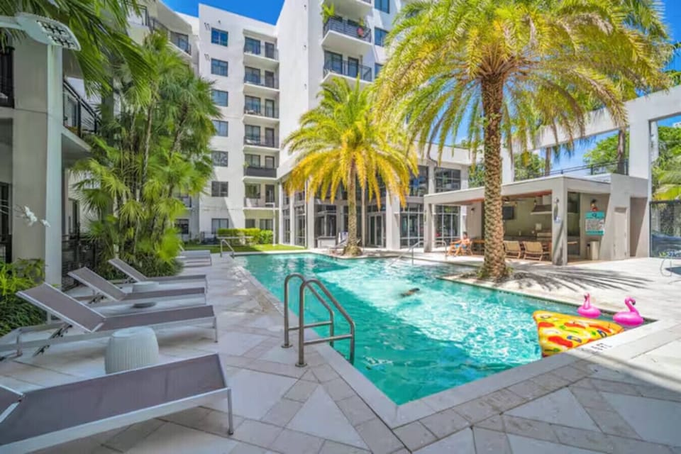 Resort-Style Pool Area-Tropical courtyard pool surrounded by palm trees, lounge chairs, and shaded seating areas. Perfect for sunbathing, swimming, or relaxing in a vibrant setting.