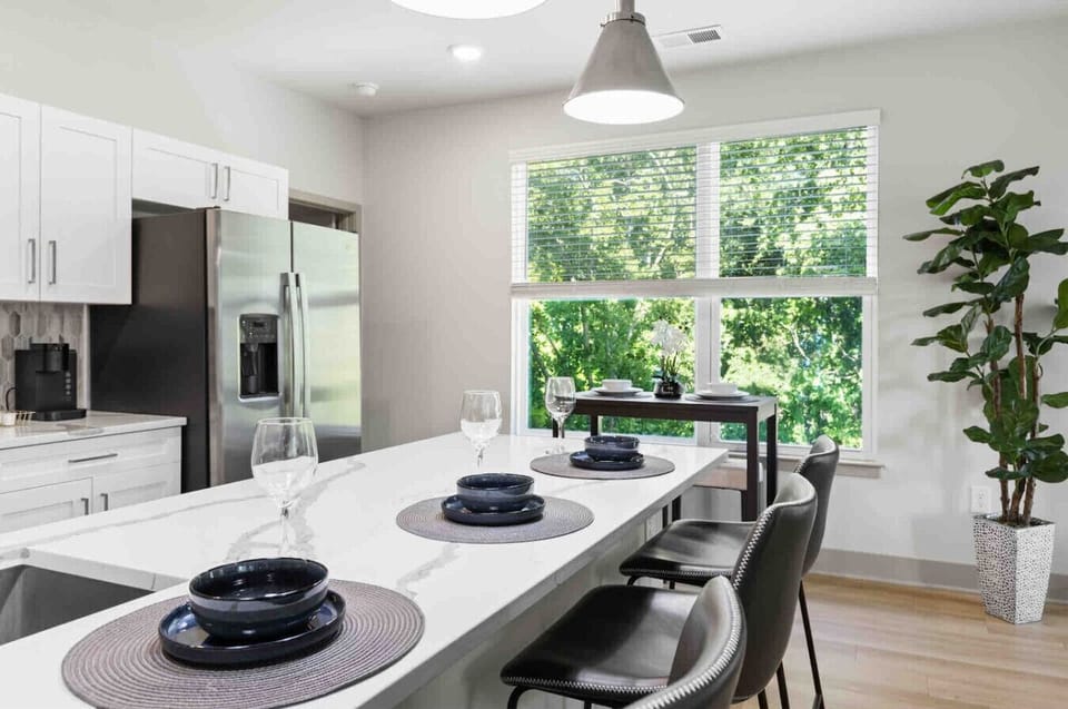 Bright Kitchen with Island Seating-Modern kitchen featuring sleek white cabinetry, stainless steel appliances, and a spacious island set for dining. Large windows provide plenty of natural light and a fresh, airy feel.