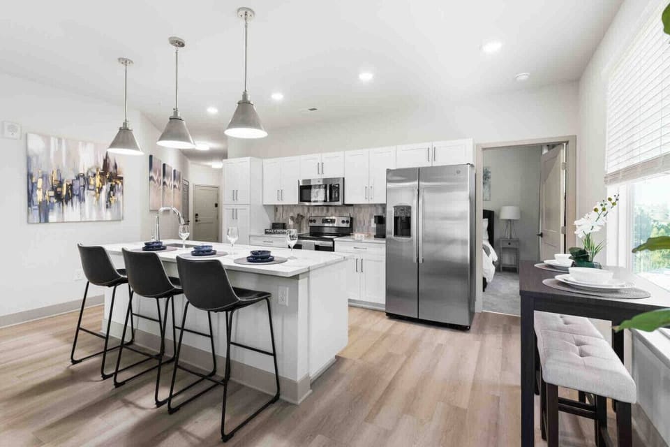 Modern Kitchen with Sleek Design-Open kitchen with stainless steel appliances, bright white cabinetry, and a central island with bar seating. Pendant lights and wood flooring add warmth and style to the contemporary space.