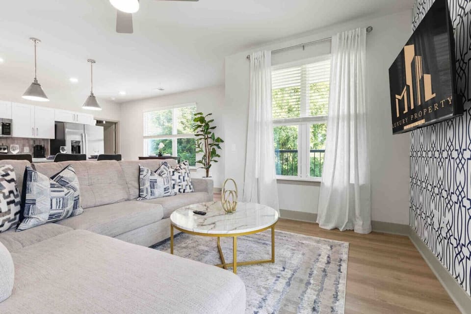 Cozy Modern Living Room-Inviting space with a plush sectional sofa, patterned pillows, and a chic marble coffee table. Large windows with flowing curtains fill the room with natural light for a bright, relaxing ambiance.