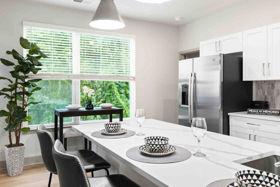 Modern Kitchen with Bright Dining Space- Sleek kitchen with stainless steel appliances, white cabinets, and a sunlit dining area. Perfect for home-cooked meals and entertaining, offering comfort and style for your stay.