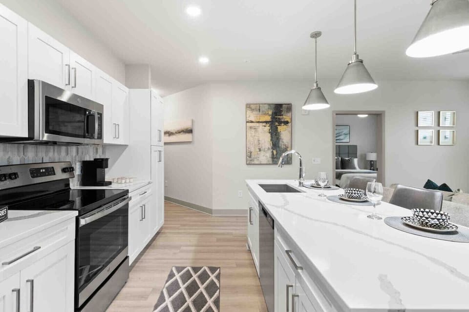 Modern Kitchen with Island Seating- Bright and spacious kitchen featuring sleek white cabinets, stainless steel appliances, and a large island with seating. Perfect for cooking, dining, and gathering in a stylish and functional space.