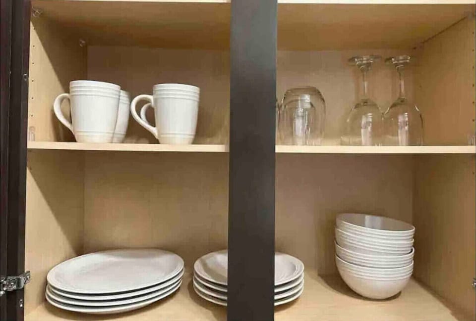 Kitchen Cabinet Essentials- Organized cabinet with mugs, wine glasses, plates, and bowls, providing all the basics for meals and drinks during your stay.