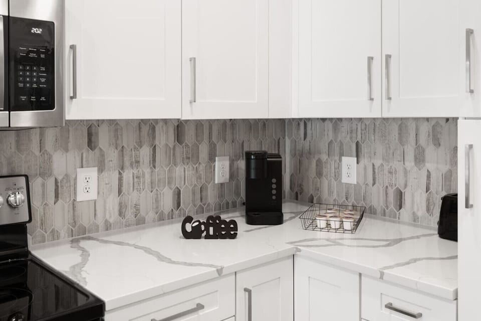 Coffee Corner-Modern kitchen nook with sleek white cabinets, marble countertops, and a stylish backsplash. Equipped with a coffee maker and pods, it’s the perfect spot to start your mornings with ease.