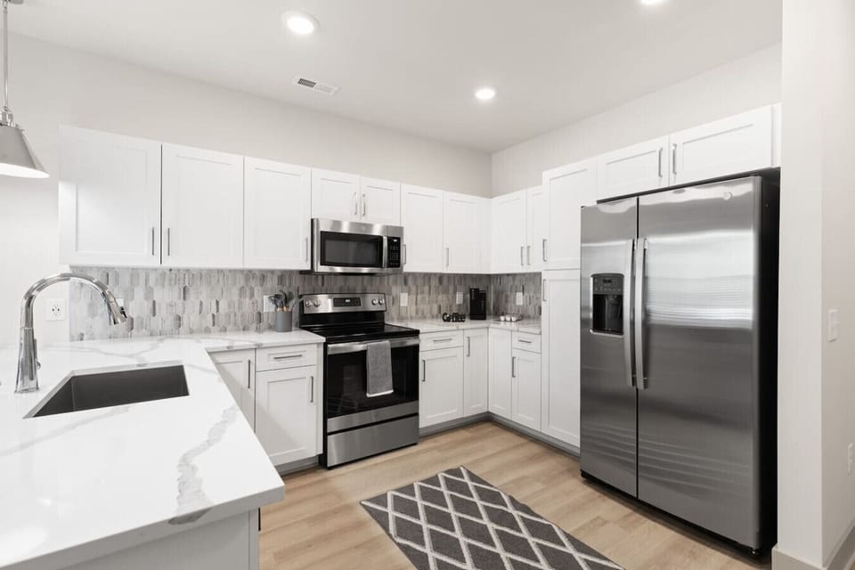 Modern Kitchen Design-Sleek kitchen featuring stainless steel appliances, white cabinetry, and a stylish backsplash. Pendant lighting and a spacious island with seating make it ideal for cooking, dining, and entertaining.