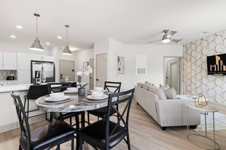 Dining & Kitchen View-Elegant dining table set for four with a marble top, overlooking the open kitchen and cozy living area. Bright lighting and modern décor create a welcoming space for meals and gatherings.