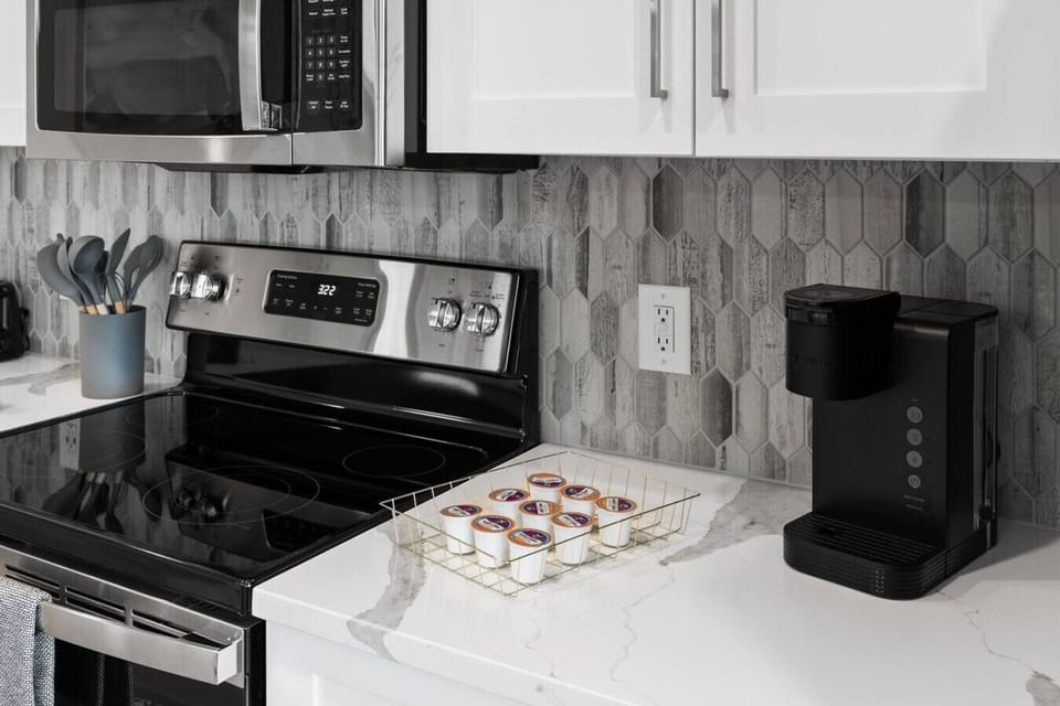 Modern Kitchen Essentials-Sleek kitchen setup with stainless steel appliances, stylish backsplash, and coffee maker with pods ready for guests. Perfect for convenient cooking and a fresh morning start.