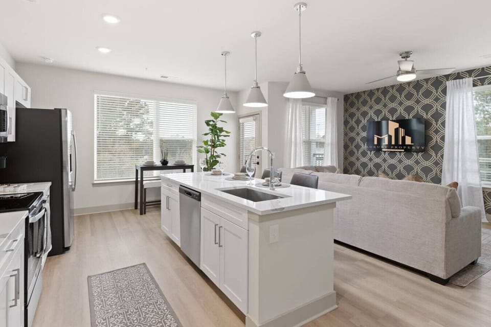 Open Kitchen & Living Area-Bright and airy space featuring a sleek kitchen island, stainless steel appliances, and cozy living area with modern décor. Large windows fill the room with natural light, perfect for cooking and entertaining.