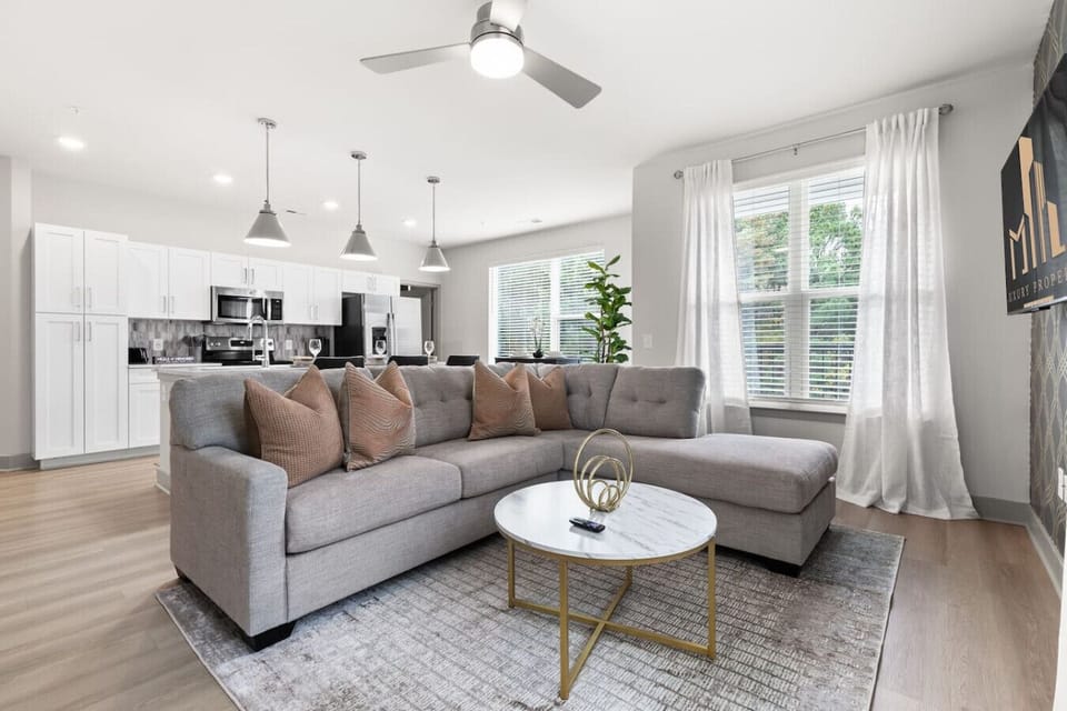 Cozy Modern Living Room-Spacious lounge with a sleek sectional sofa, chic décor, and bright natural light. Open layout connects to the kitchen, creating a perfect space for relaxation, conversation, and entertaining.