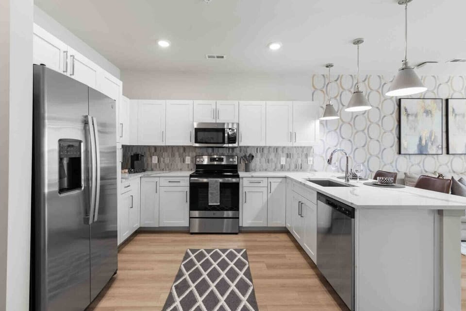 Modern Chef’s Kitchen-Spacious kitchen with stainless steel appliances, sleek white cabinetry, and stylish lighting. Features a large countertop, dishwasher, and open layout ideal for cooking and entertaining.