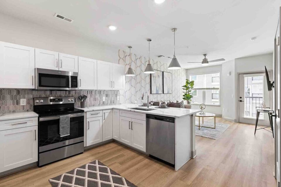 Open-Concept Kitchen-Modern kitchen with stainless steel appliances, white cabinetry, and stylish backsplash. Overlooks the living area with natural light, creating a bright and inviting open layout.