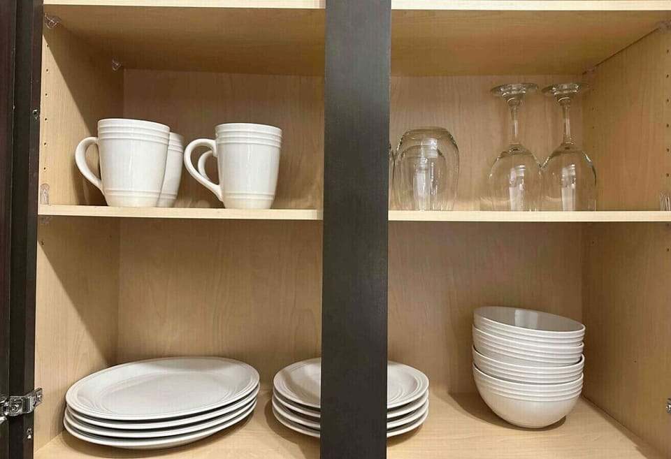 Fully Stocked Cabinet-Kitchen cabinet with mugs, plates, bowls, and glassware neatly arranged. Everything you need for dining and enjoying meals at home during your stay.