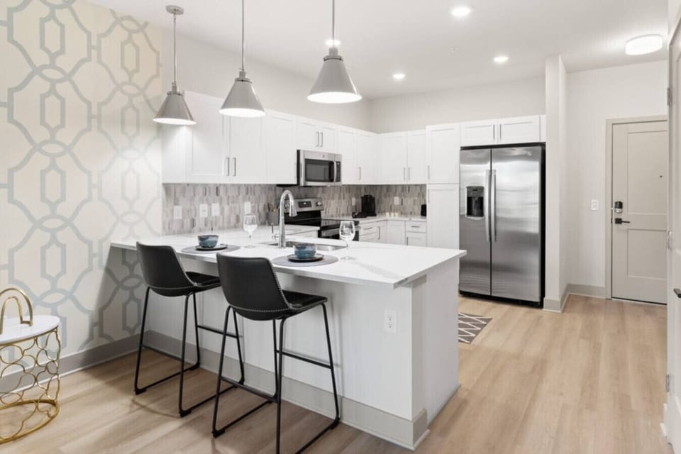 Kitchen with Breakfast Bar-Modern kitchen with stainless steel appliances, white cabinetry, and stylish backsplash. Features a spacious island with bar seating, perfect for dining or entertaining.