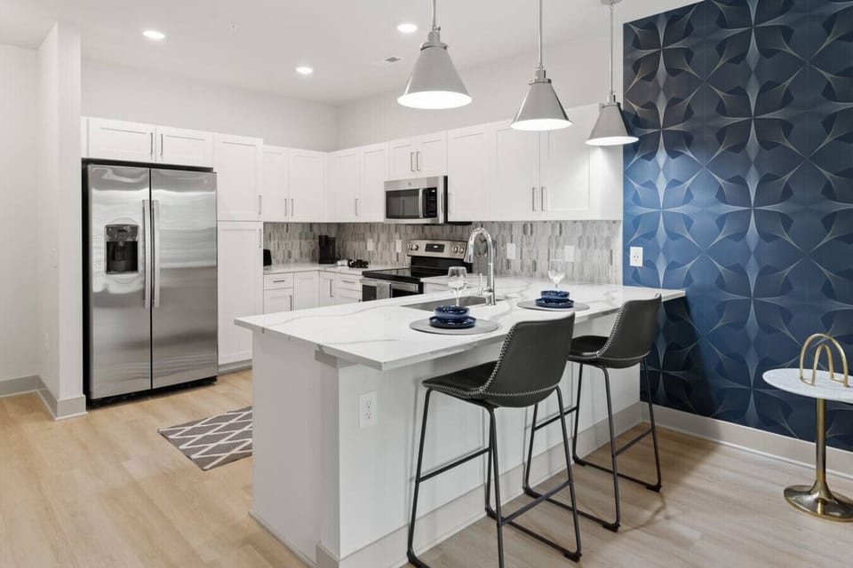 Kitchen with Breakfast Bar-Modern kitchen with stainless steel appliances, white cabinetry, and stylish backsplash. Features a spacious island with bar seating, perfect for dining or entertaining.